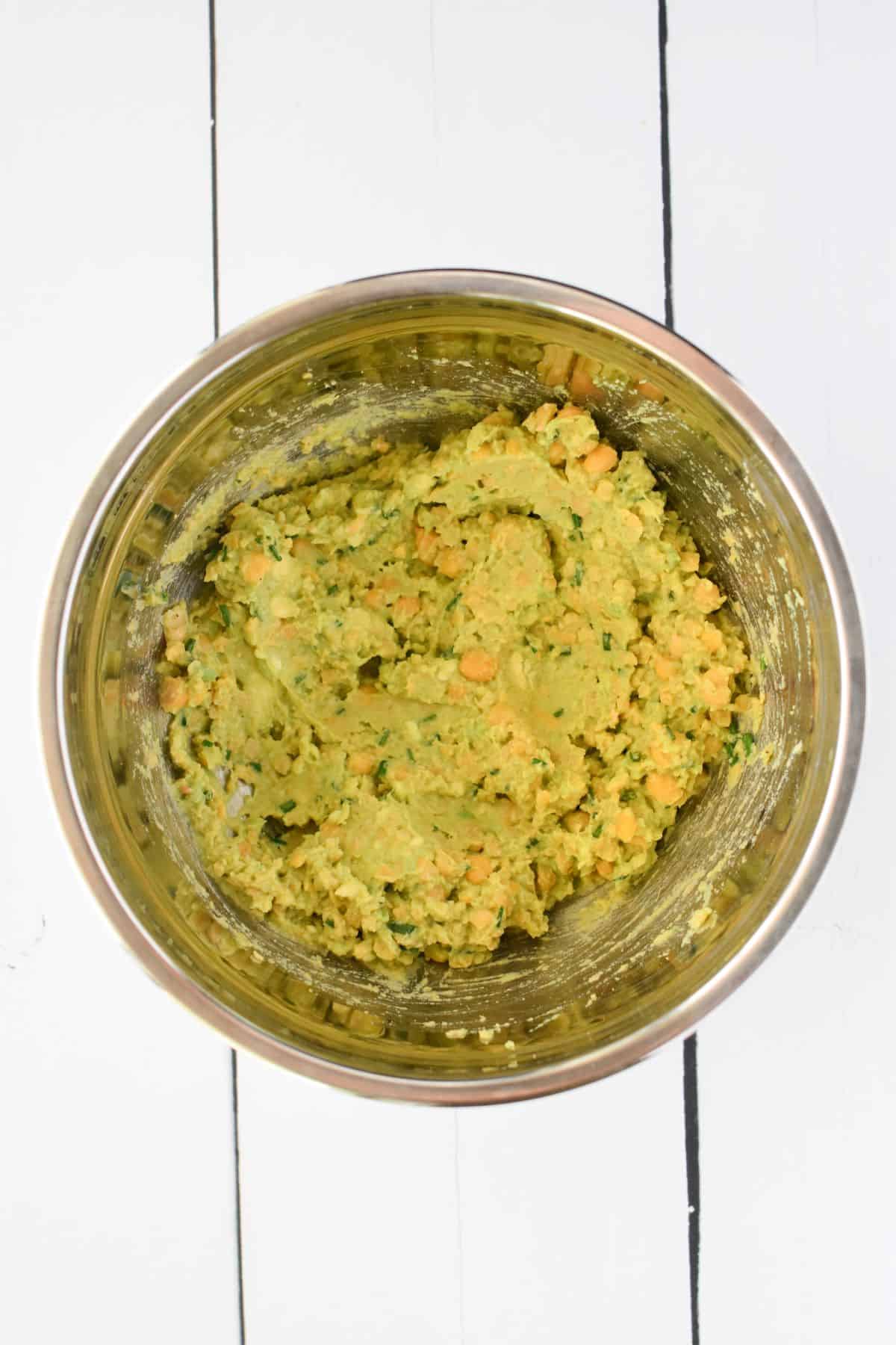 Avocado mixed into chickpeas in a bowl overhead view.