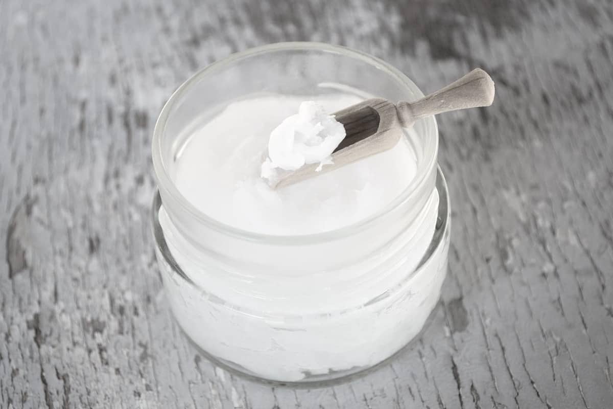 coconut oil in a jar with some on a wooden scoop.