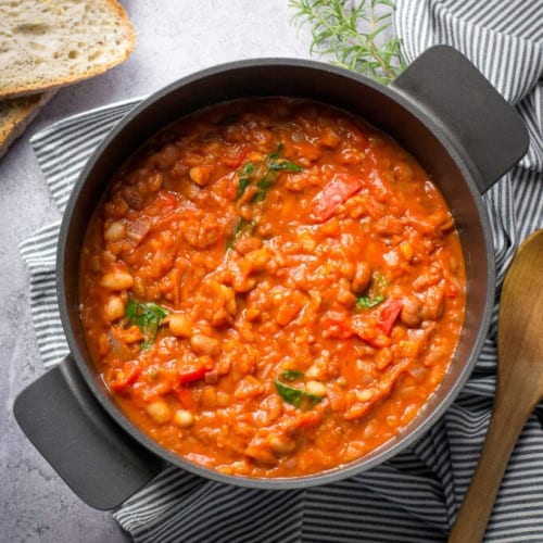 Tuscan bean stew in a pot with a wooden spoon.