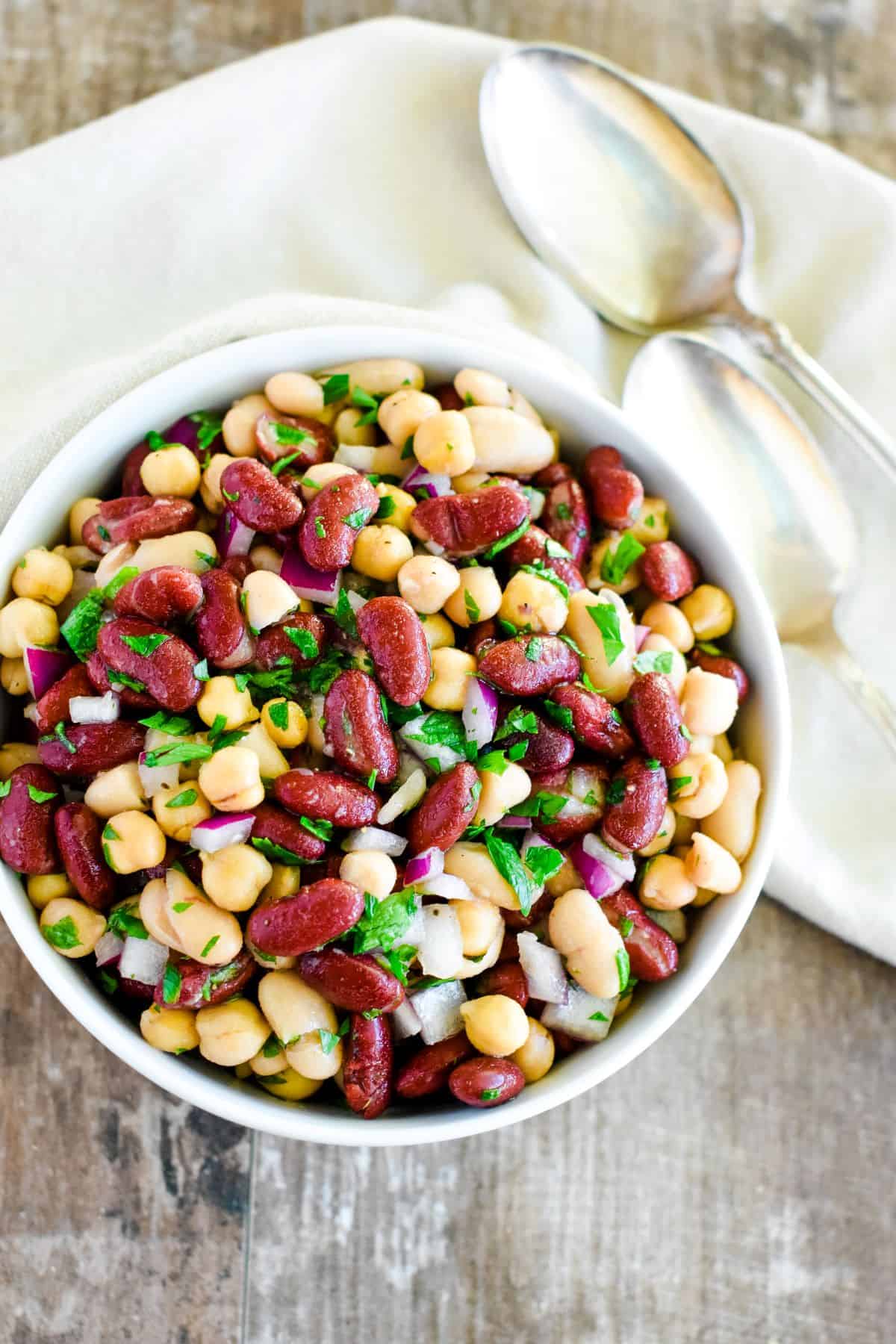 overhead of bean salad in a white bowl with a spoon next to it on the right.