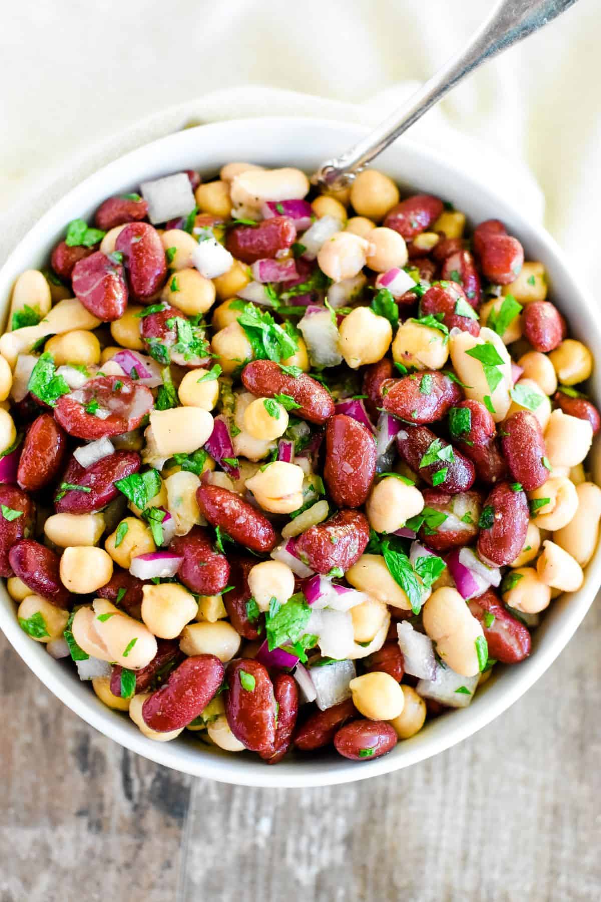 overhead of bean salad in a white bowl with a spoon in it.