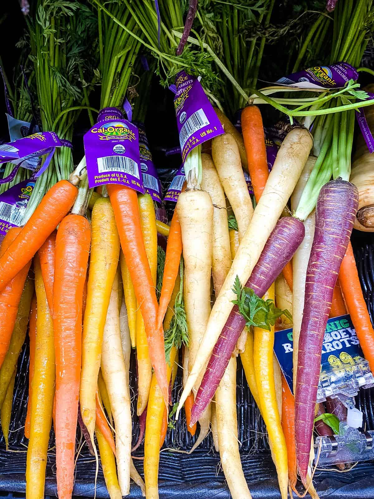 Tri-colored carrots in basket on supermarket shelf.