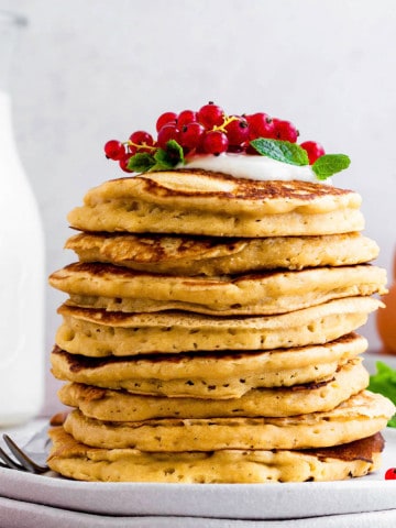 A stack of almond milk pancakes topped with red grapes, yogurt, and mint leaves, placed on two stacked white plates.