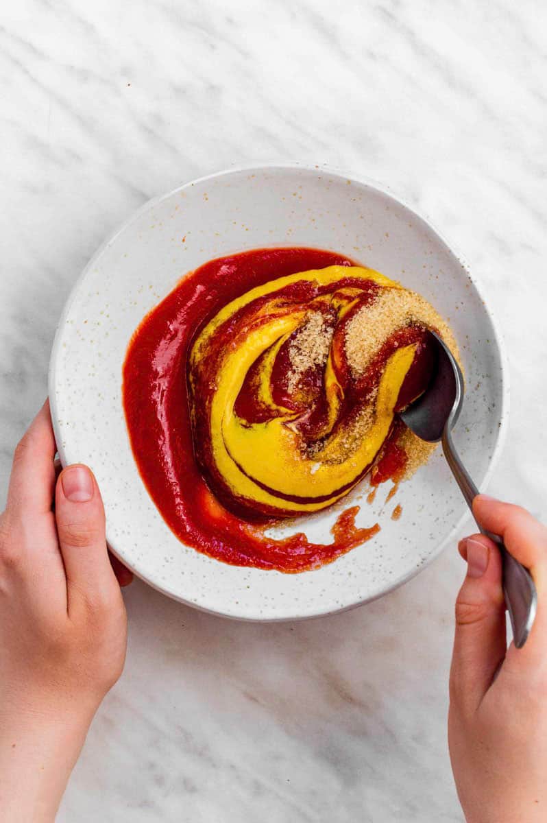 Two hands mixing ketchup glaze with a spoon.