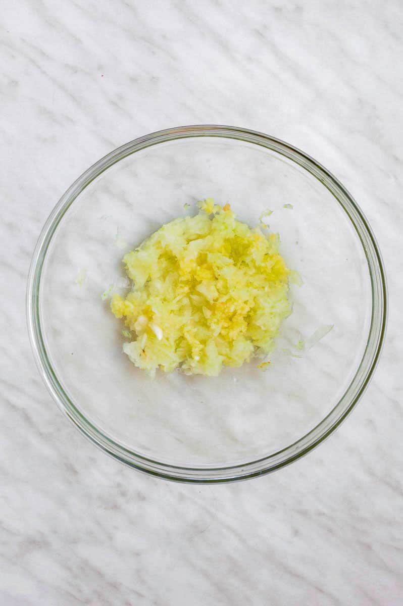 Shredded onion and minced garlic in w clear mixing bowl.