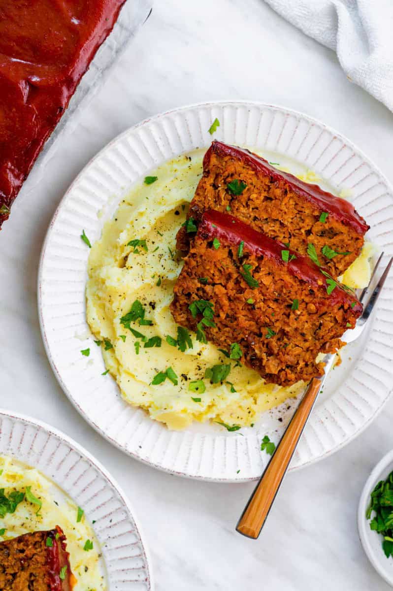 A white plate filled with mashed potatoes and two pieces of Beyond meat meatloaf.