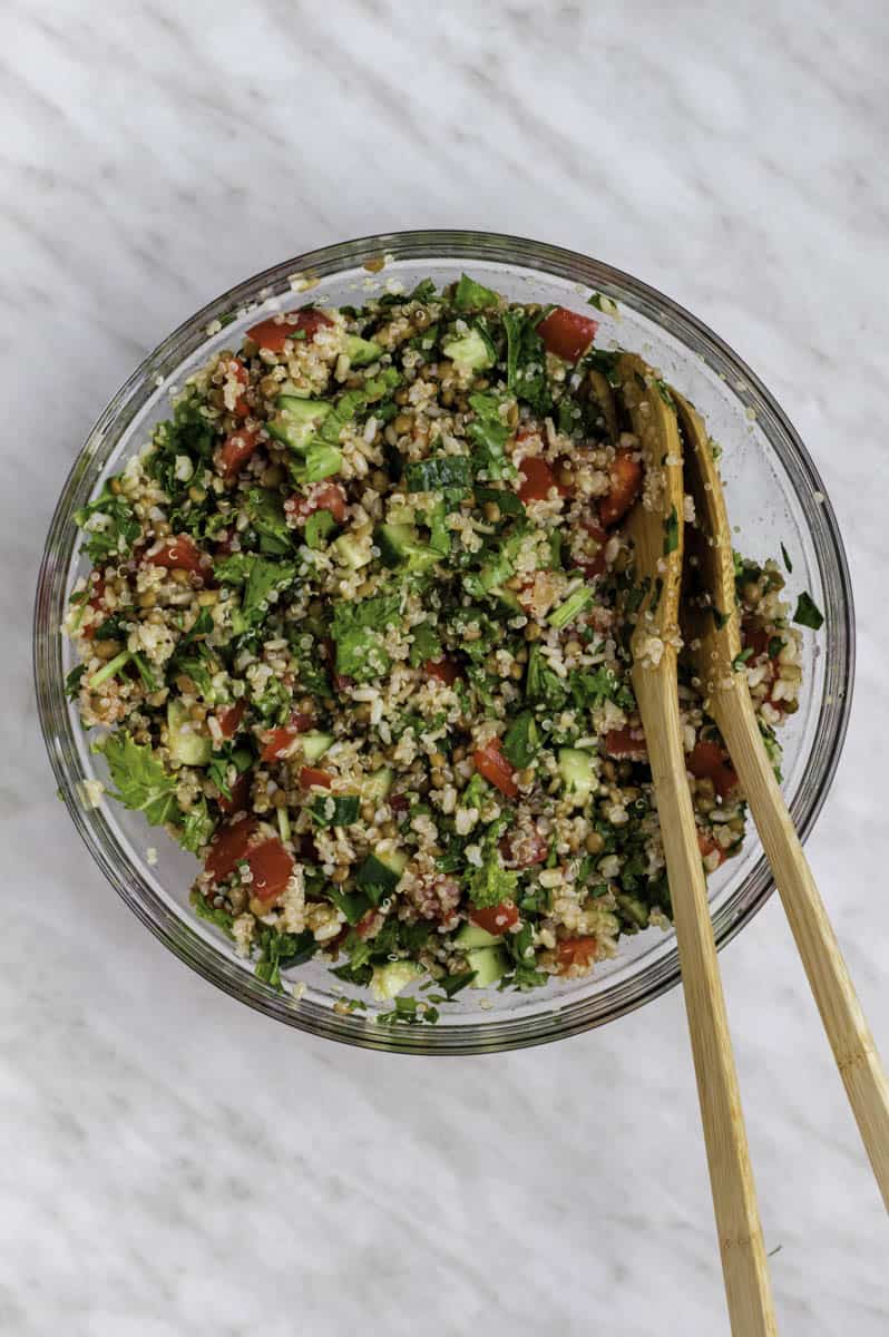 Copycat Costco quinoa salad in a glass mixing bowl with two wooden spoons in it.