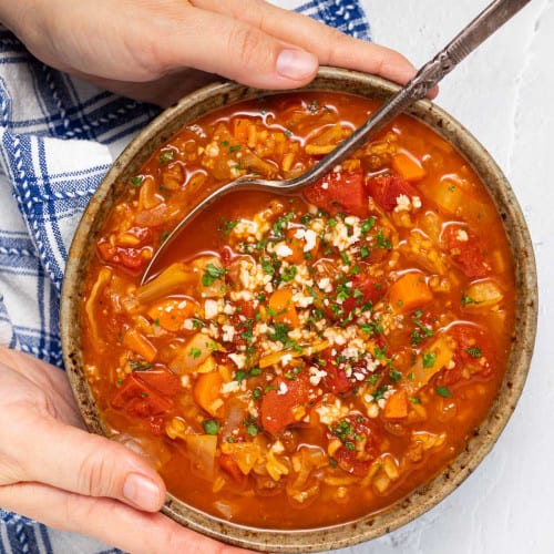 Hands holding a bowl of Vegan Cabbage Soup with a spoon.