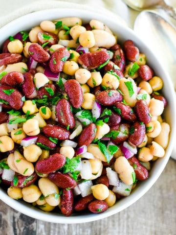 close-up of bean salad in a white bowl with spoons to the right.