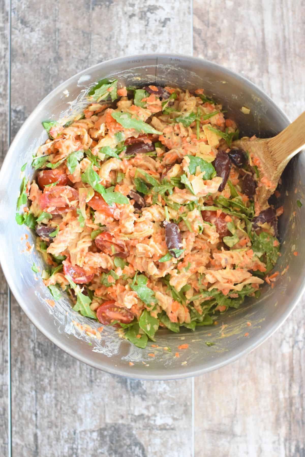 overhead of pasta salad after being mixed in a mixing bowl with a wooden spoon.