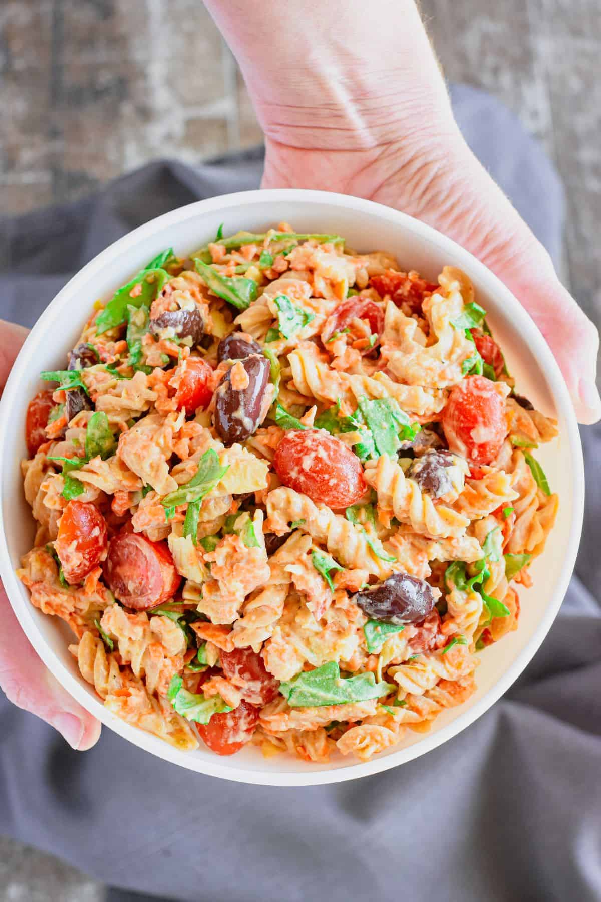 overhead of hummus pasta salad in a bowl being held up by two hands.