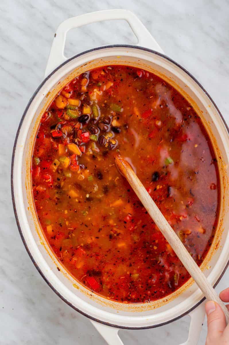 Stirring black bean soup with a wooden spoon from a Dutch oven.