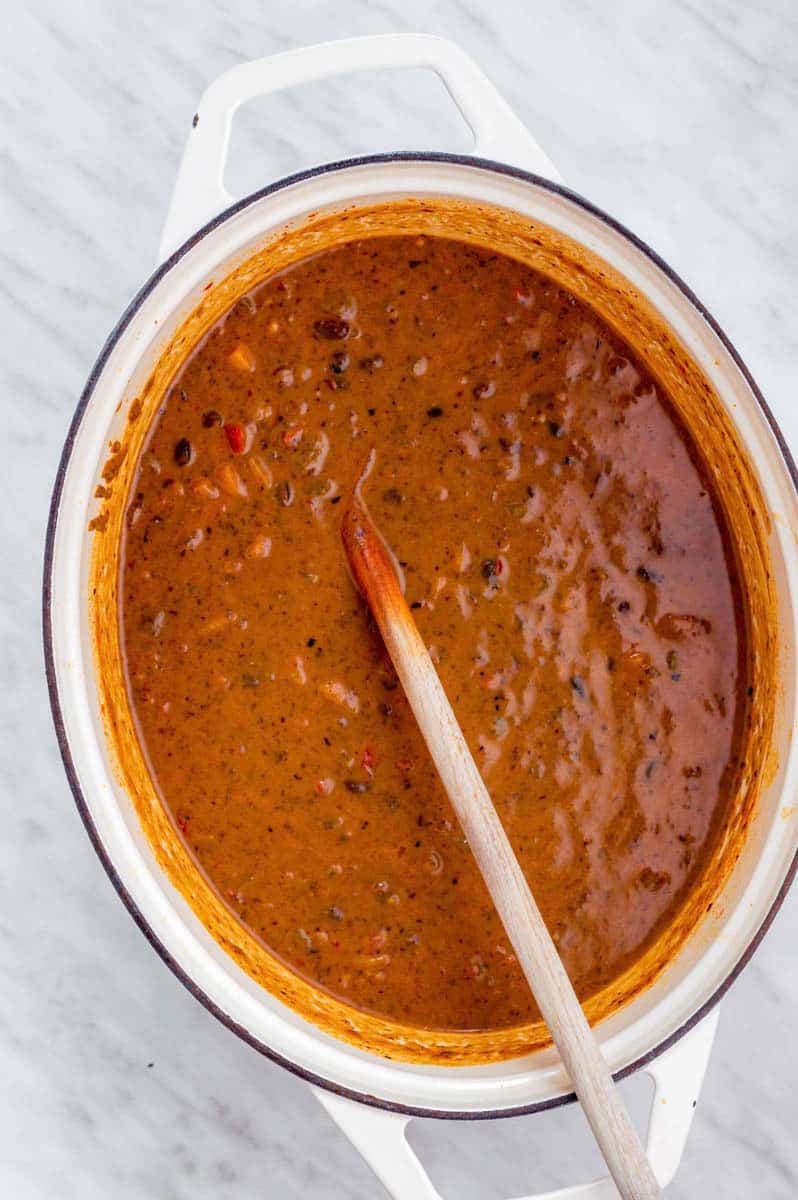 Panera bread black bean soup in a white Dutch oven with a large wooden spoon in it.