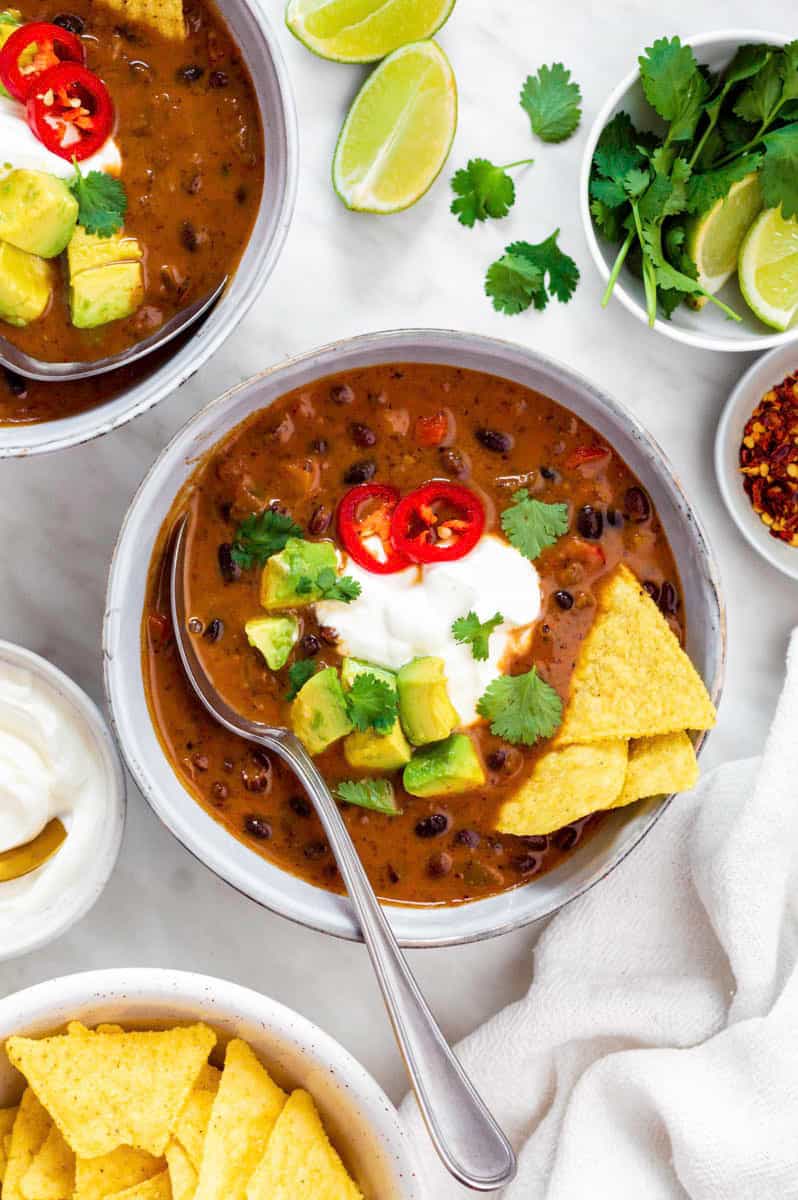 Panera bread black bean soup in a blue bowl, topped with sour cream, avocado, cilantro and tortilla chips.