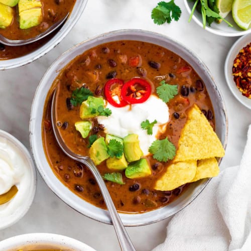 Panera bread black bean soup in a blue bowl, topped with sour cream, avocado, cilantro and tortilla chips.