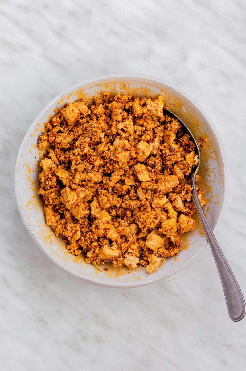 Crumbled tofu mixed with the soy paste in a white bowl with a spoon in it.