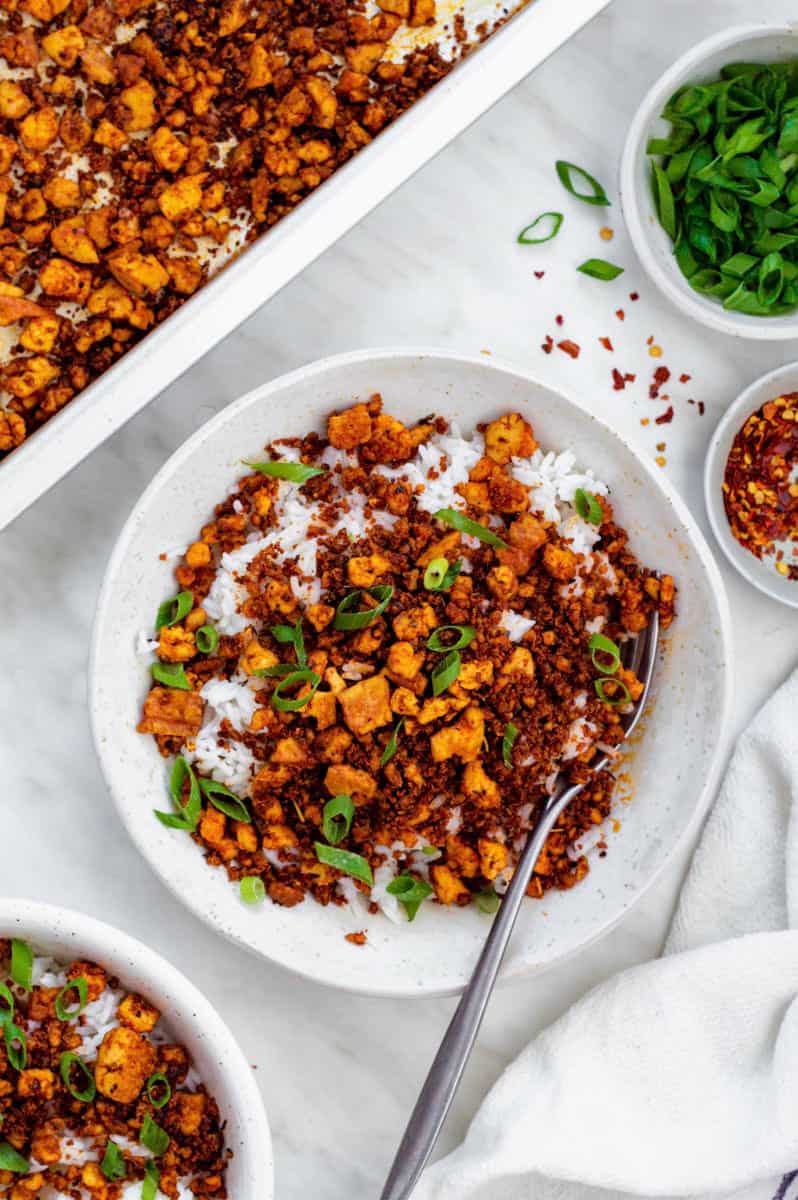 A white bowl filled with cooked white rice topped with tofu ground beef and chopped green onion.