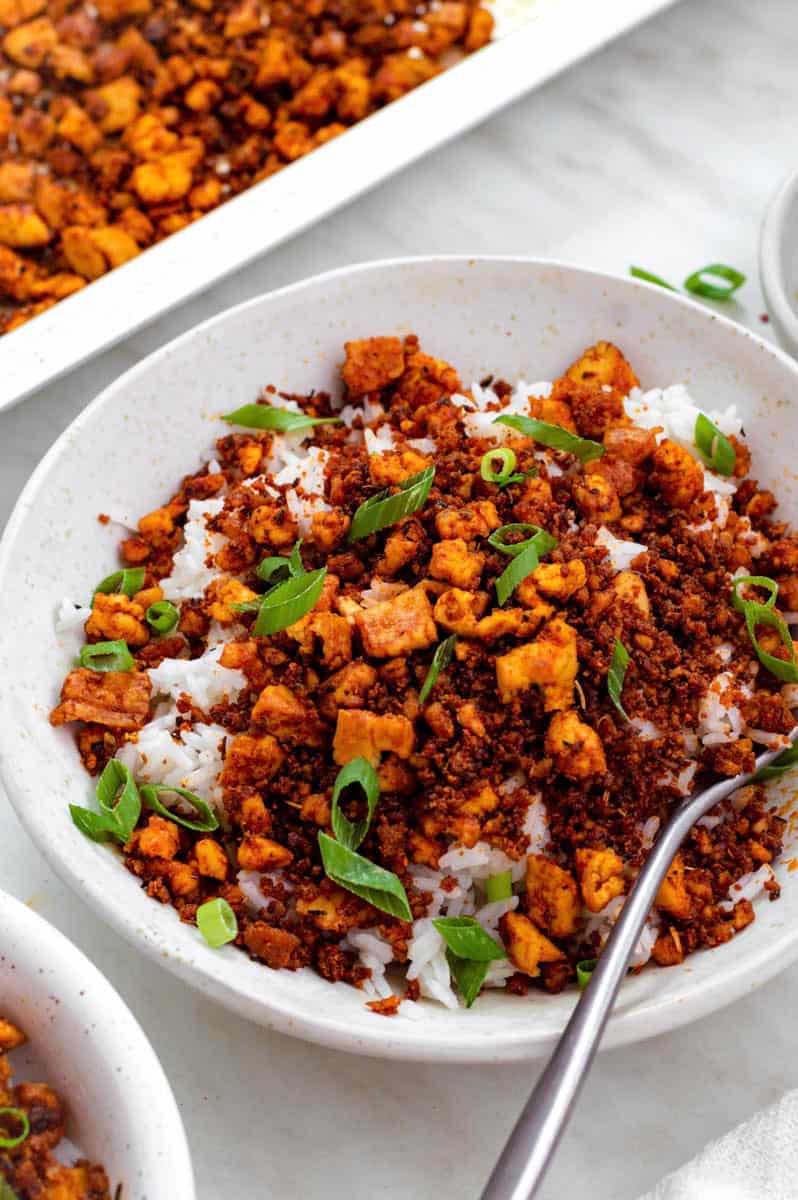 A white bowl filled with rice and tofu beef crumbles, topped with chopped green onion. A fork placed on the right side of the bowl.