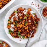 A white bowl filled with cooked white rice topped with tofu ground beef and chopped green onion.