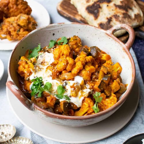 eggplant and cauliflower curry in a bowl with herb garnish.