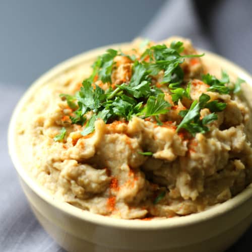 baba ghanoush hummus with herb garnish in a white bowl on a kitchen towel.