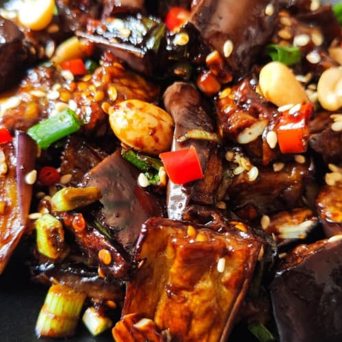 close-up of Chinese eggplant in garlic sauce in a black bowl.