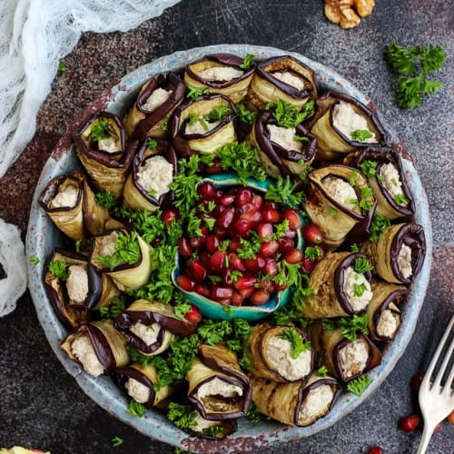 overhead of Georgian eggplant rollups in a serving dish with pomegranate seed garnish in the middle.