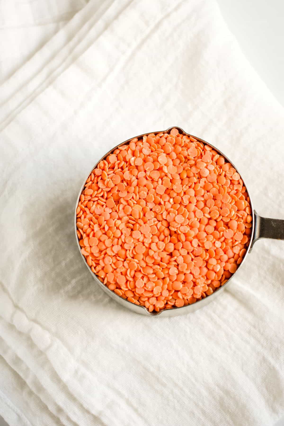 dry red lentils in a measuring cup on a white kitchen towel.