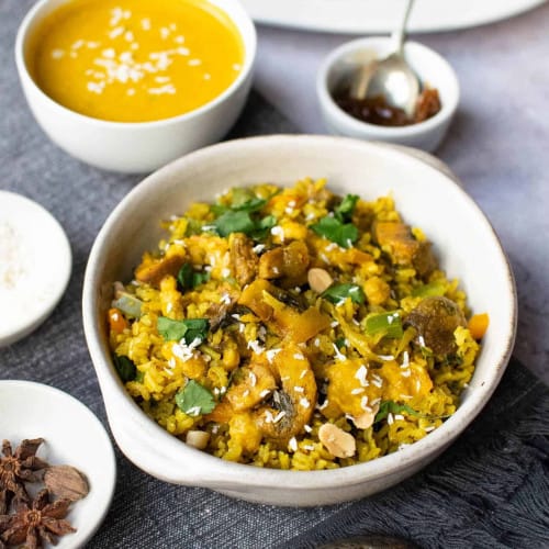 overhead of mushroom biryani in a white bowl with garnishes around.