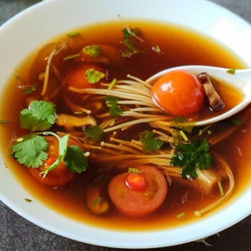 vegan tom yum soup in a white bowl with a white spoon scooping some out.