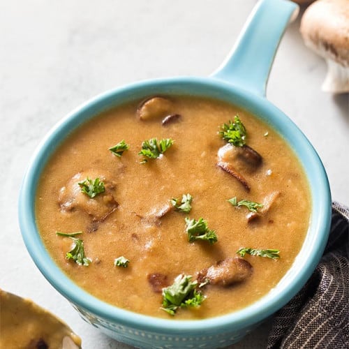 vegan mushroom gravy in a blue serving bowl with spoon in the front of it.