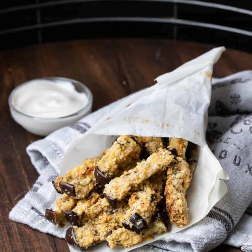 baked eggplant fries in a paper cone on a kitchen towel.