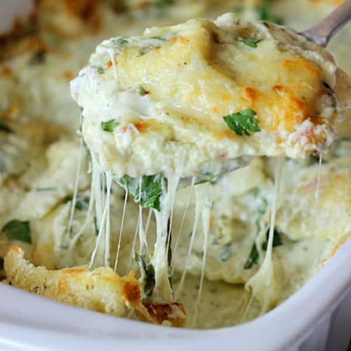 A spoon scooping a serving of ravioli casserole with cheese.