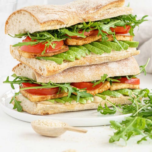 Two tofu sandwiches on a plate with lettuce leaves in front.