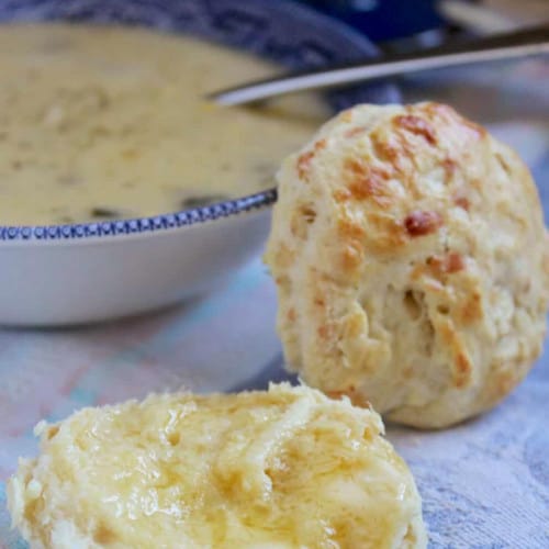 Homemade savory scones in front of a bowl of broccoli cheese soup.