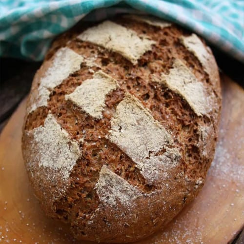 Beer bread on a dark wood cutting board with blue towel in back.