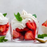 A small glass cup filled with halved strawberries topped with dairy-free whipped cream and fresh mint leaves.