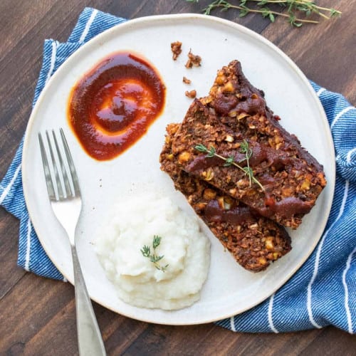 three slices of lentil loaf with mashed potatoes and a fork on a white plate.