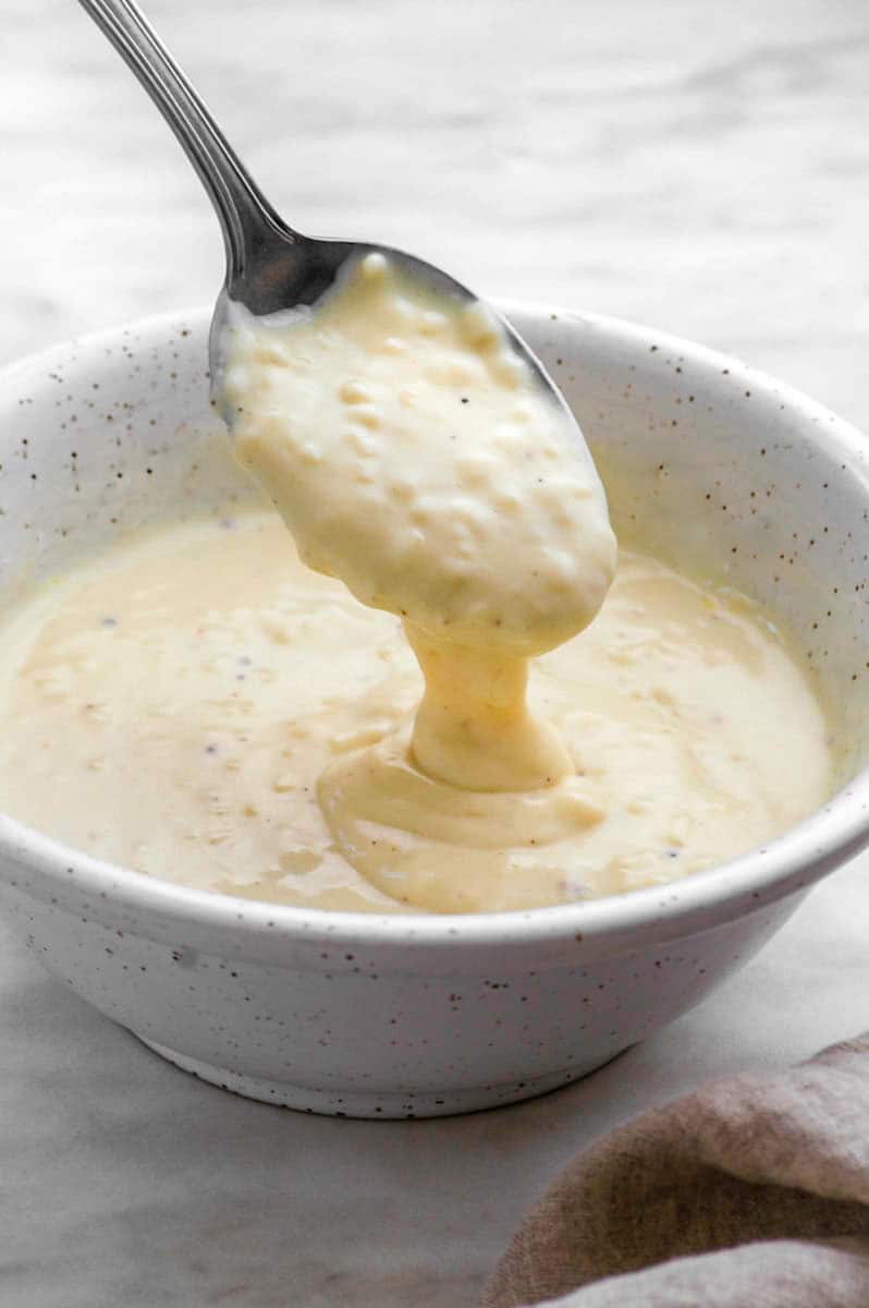 A white bowl filled with garlic pizza sauce with a spoon dipping into it.