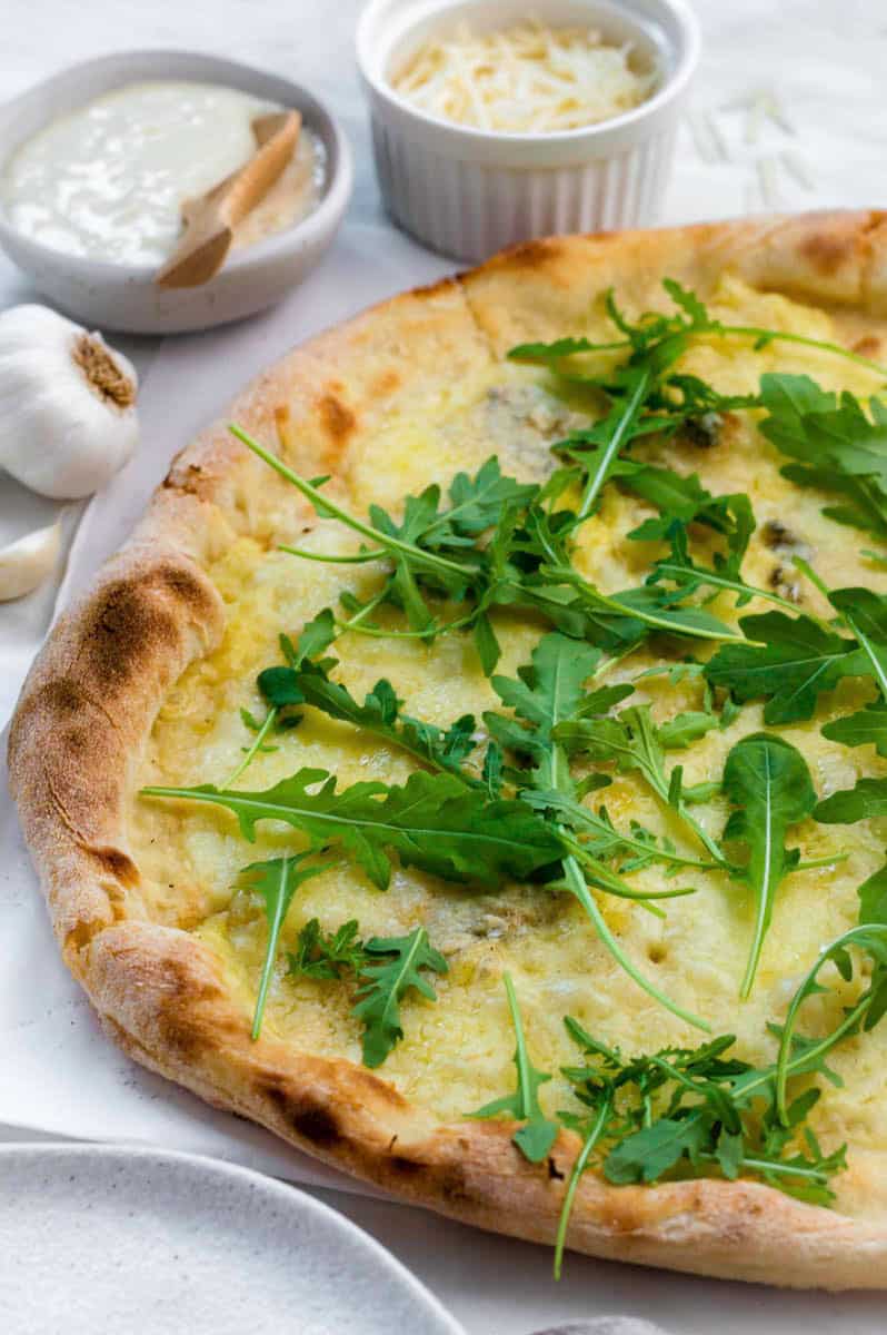 Four cheese pizza topped with arugula served on a piece of parchment paper.