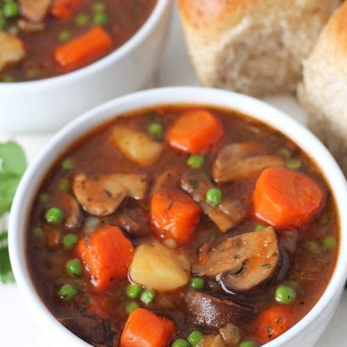 mushroom stew in a white bowl with rolls and another bowl behind it.