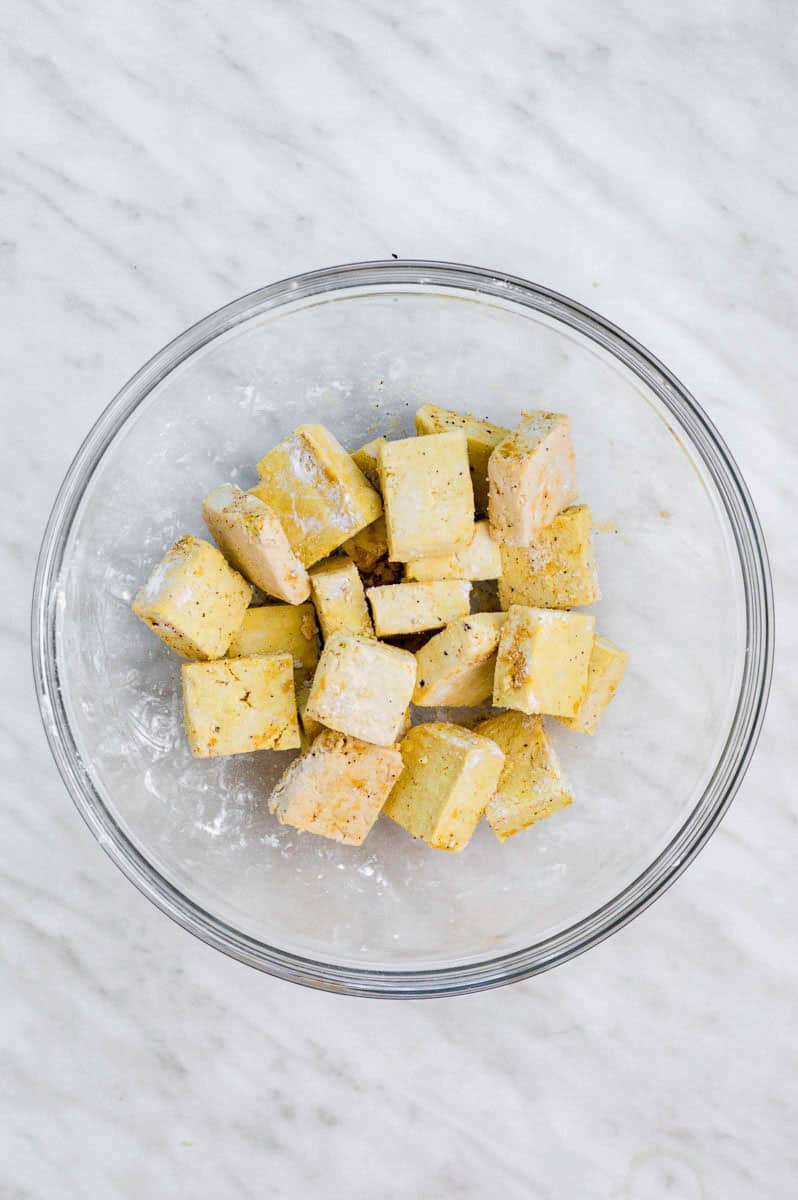 Tofu cubes tossed in corn starch and spices in a clear mixing bowl.