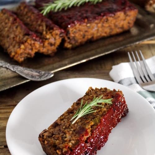 slice of mushroom walnut loaf on a white plate with the rest behind it.