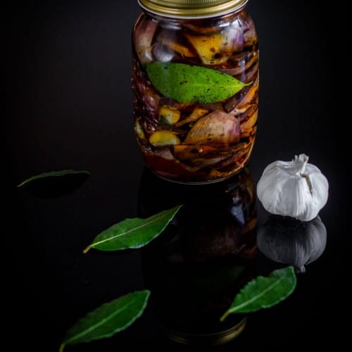 front view of pickled eggplant in a mason jar on a black surface.