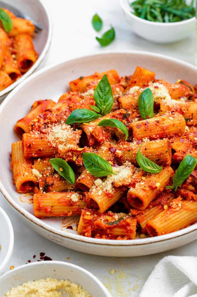 Tofu tomato pasta served in a white plate and topped with basil, vegan parmesan, and red pepper flakes.