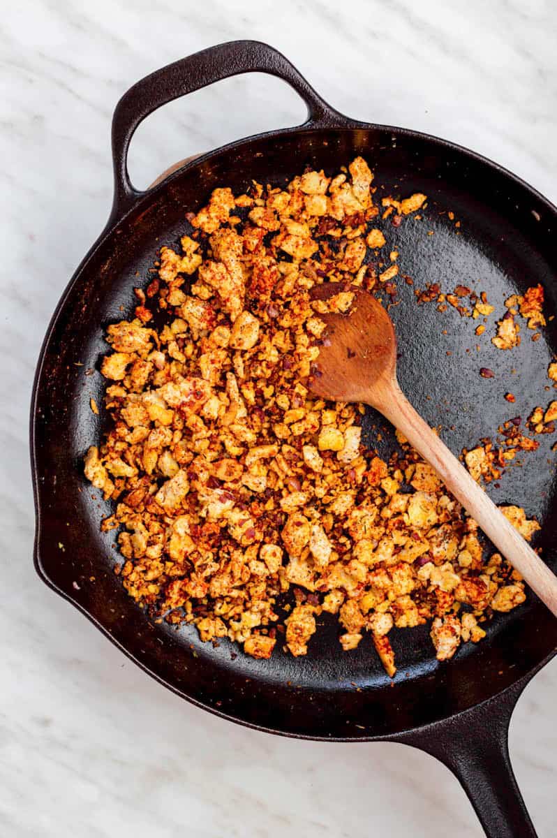 Frying crumbled tofu in a black cast-iron skillet.