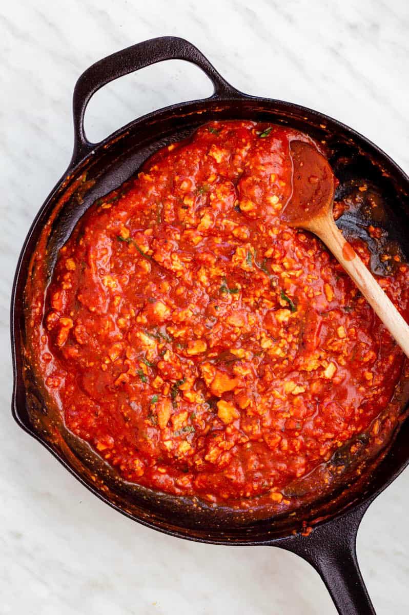 Tomato sauce with tofu in a cast-iron skillet with a wooden spoon in it.