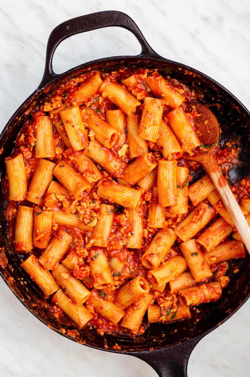 Tofu tomato pasta in a cast-iron skillet with a wooden spoon placed in the left side of the pan.