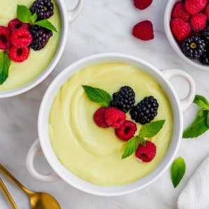 A small white bowl filled with my vegan vanilla custard recipe and topped with raspberries, blackberries and fresh mint leaves.