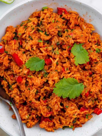 Vegan Mexican rice served in a white bowl and topped with cilantro. A silver spoon placed on the right side of the bowl.